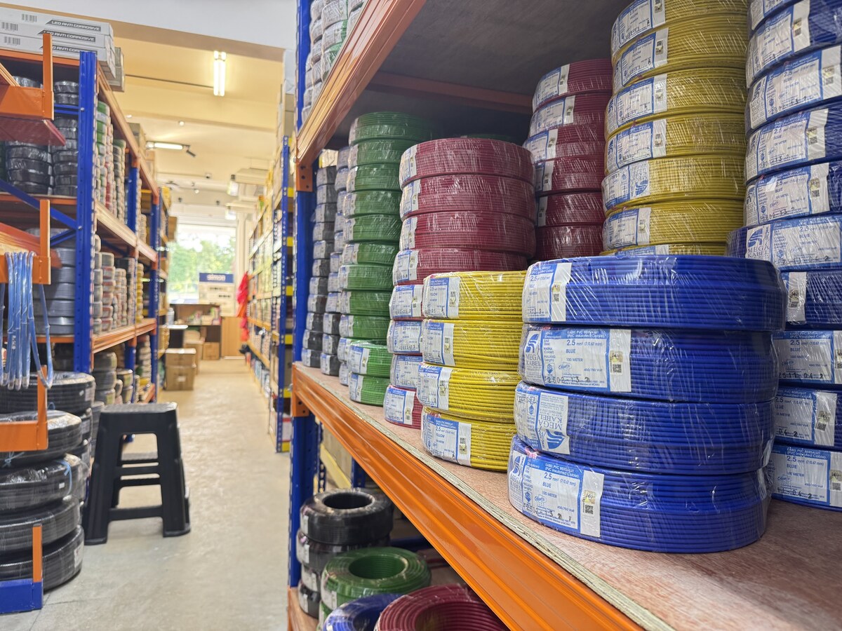 Aisle of orange and blue racking stacked with coloured coils of PVC wiring cable in plastic wrap, with Mega Kabel labels