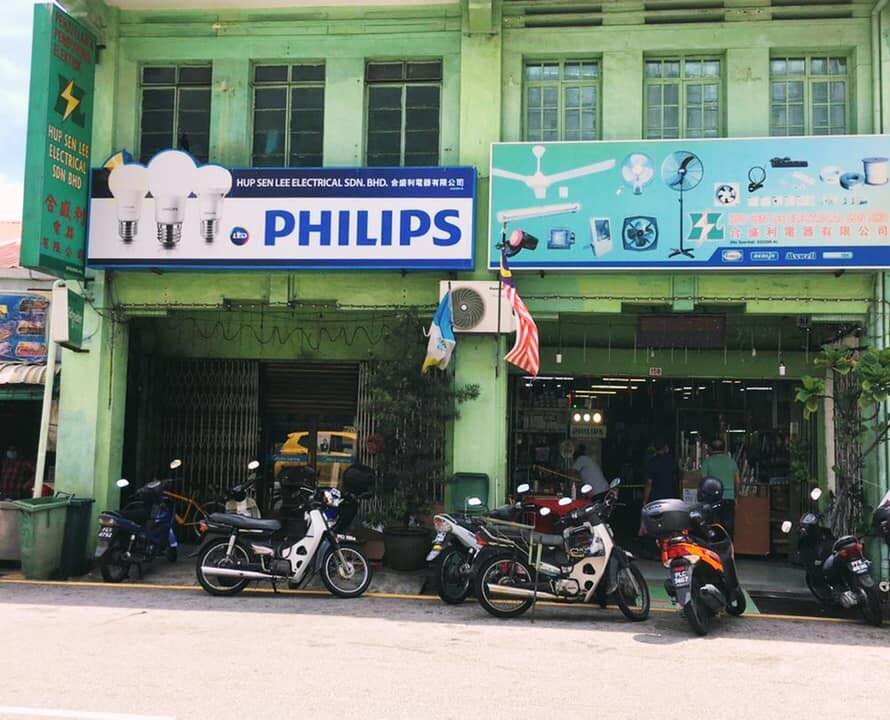 Two-storey green shophouse with a white and blue PHILIPS signboard reading Hup Sen Lee Electrical Sdn. Bhd., a light-blue signboard showing fans and lights, and motorcycles parked in front