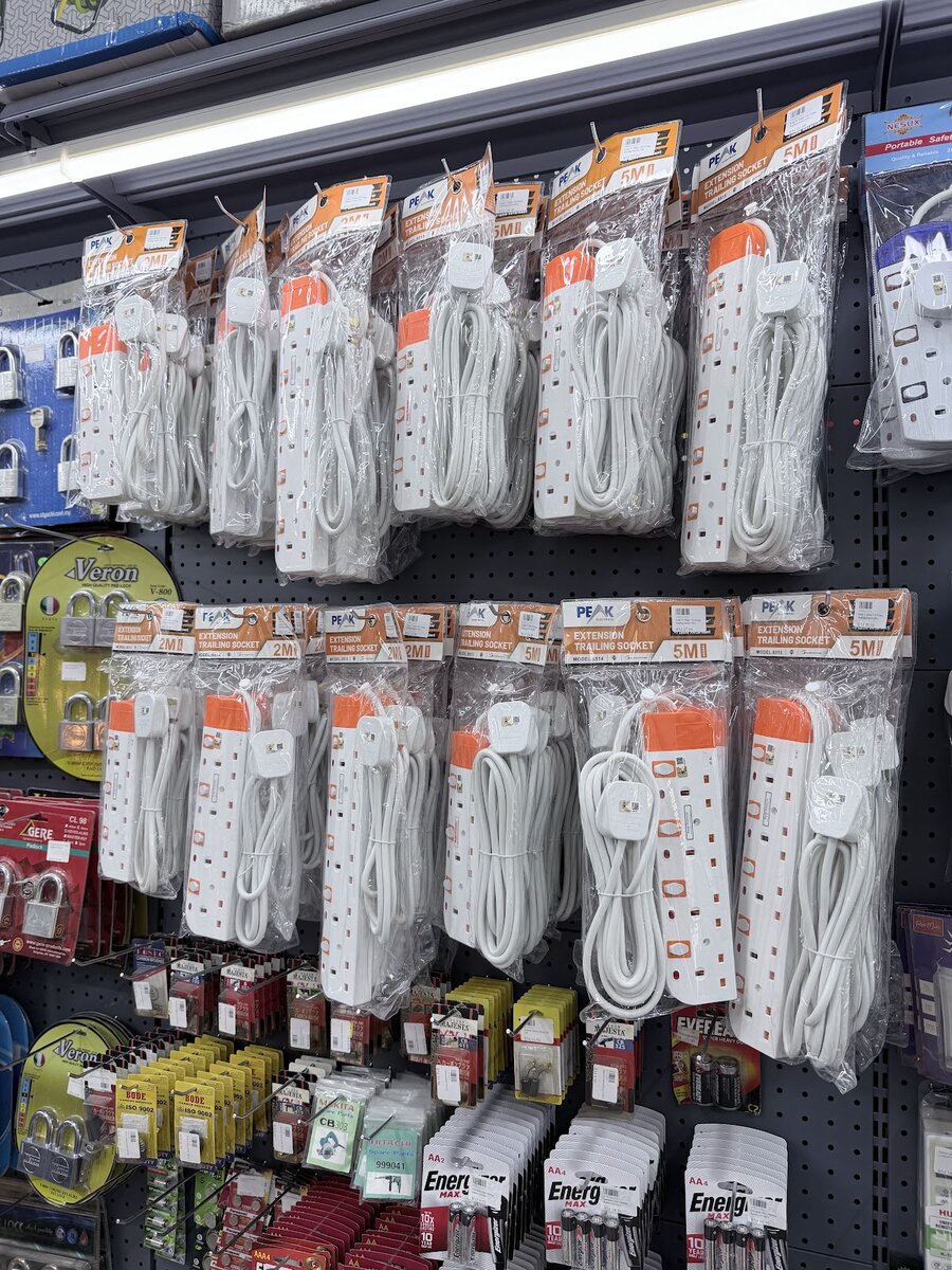Pegboard of packaged white extension trailing sockets in 2 m and 5 m lengths above padlocks and batteries