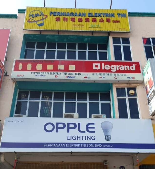 Three-storey shop building with a yellow Perniagaan Elektrik TNI sign at the top, a red and white Legrand sign in the middle and a white OPPLE Lighting signboard over the ground floor