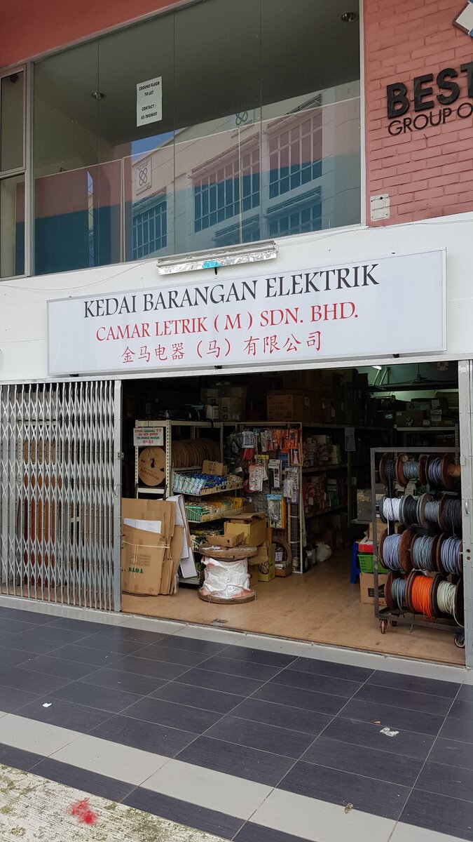 Ground-floor shop with a white "Kedai Barangan Elektrik Camar Letrik (M) Sdn. Bhd." signboard and racks of cable reels behind an open grille