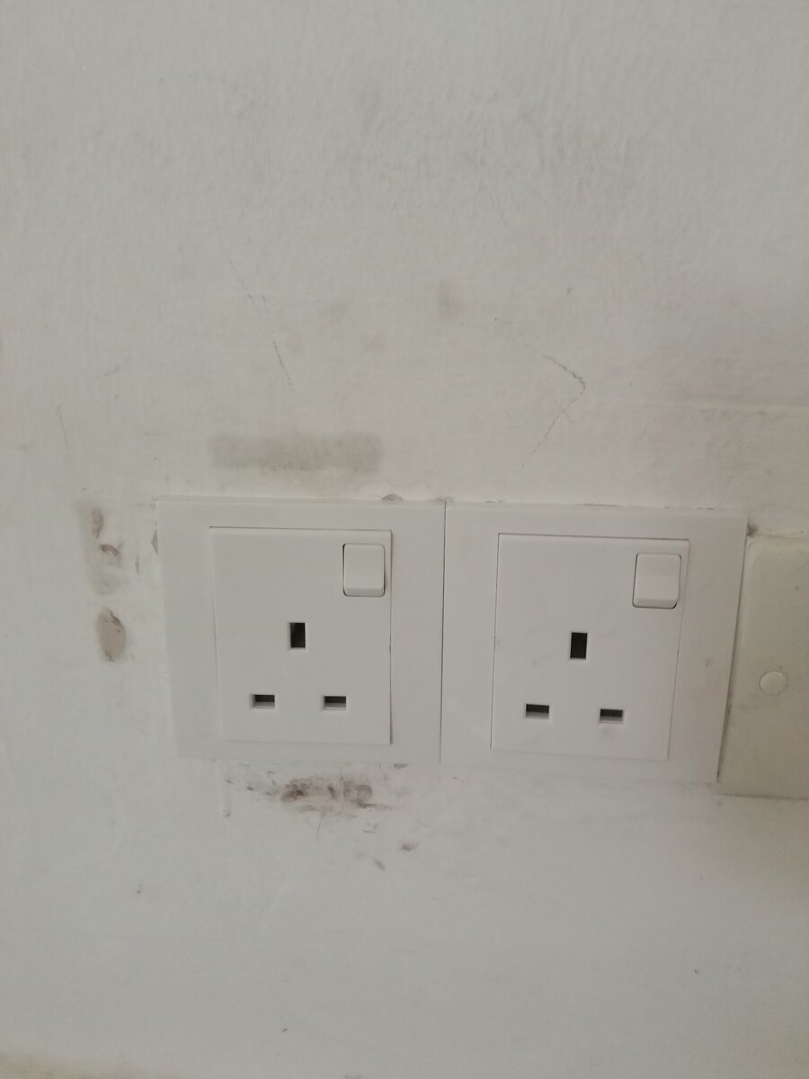 Two white switched three-pin wall sockets side by side on a white wall