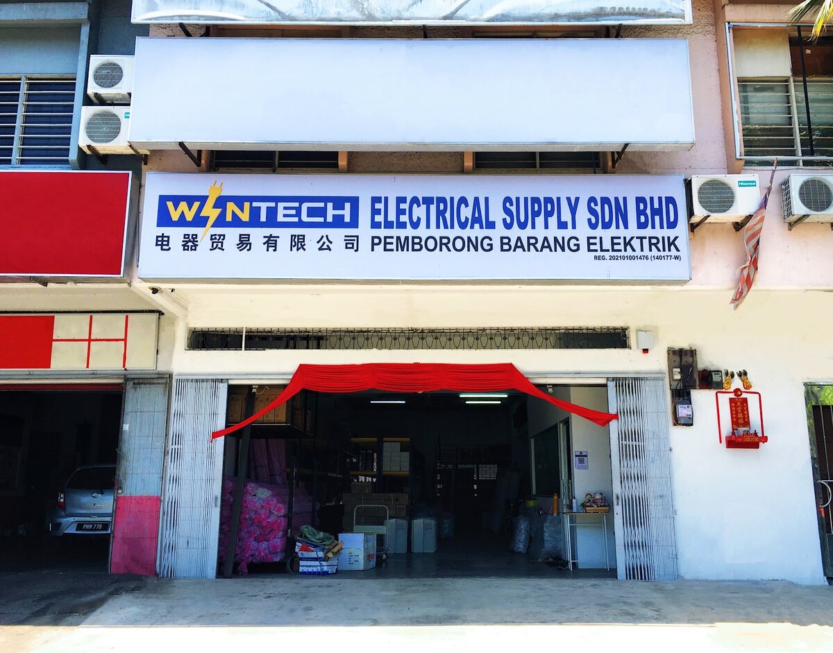 Shophouse with a white Wintech Electrical Supply Sdn Bhd signboard, an open roller-gate front with a red cloth drape and stacked goods inside