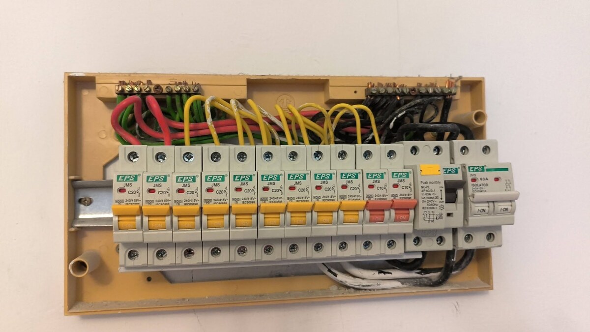 Open cream-coloured distribution board on a wall with a row of EPS miniature circuit breakers with yellow and red handles, an RCCB and a two-pole isolator, wired in red, yellow, green and black cables