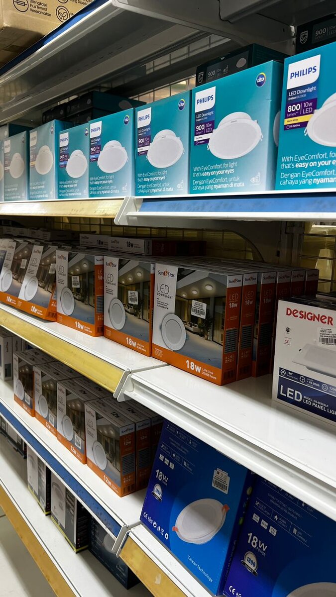 Shop shelves stacked with blue-green Philips downlight boxes on top and orange SunStar downlight boxes below
