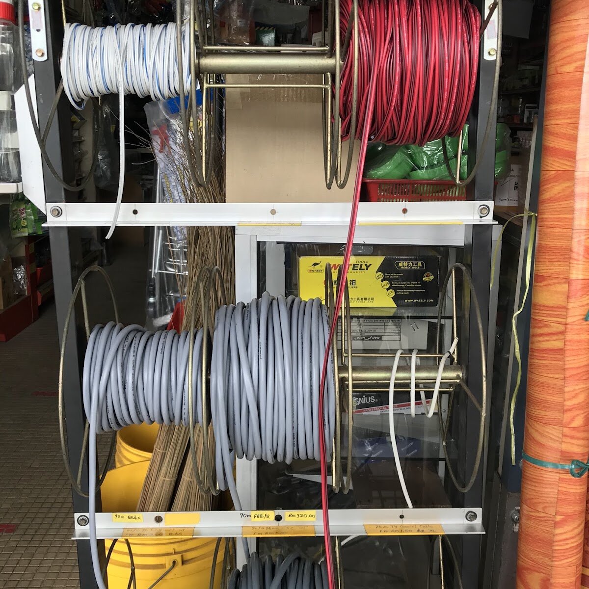Metal rack of cable reels with red-and-black twin wire, white wire and grey flexible cable, with hand-written price labels