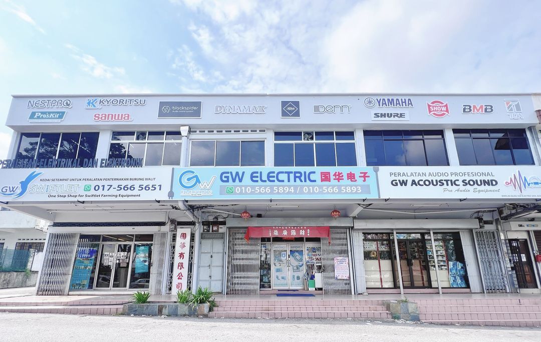 Two-storey shop row with blue and white signboards reading GW Swiftlet, GW Electric 国华电子 and GW Acoustic Sound, phone numbers, and brand logos such as Kyoritsu, Sanwa, Yamaha and TOA above
