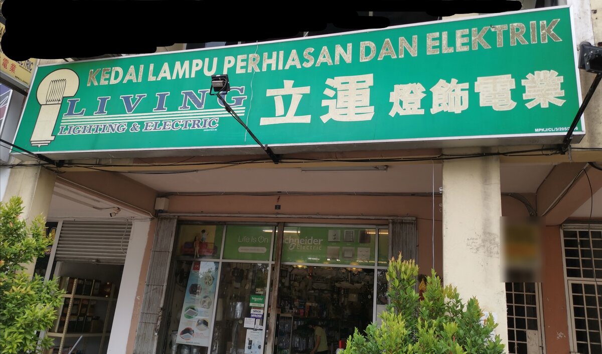 Green shop signboard with a lamp logo, the words Living Lighting & Electric and Chinese characters, over a glass shopfront with green Schneider Electric window graphics