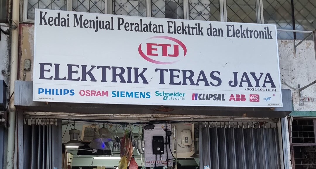 White shop signboard with a red ETJ logo, the name Elektrik Teras Jaya and a row of electrical brand logos, above an open doorway with lamps and a water-heater display