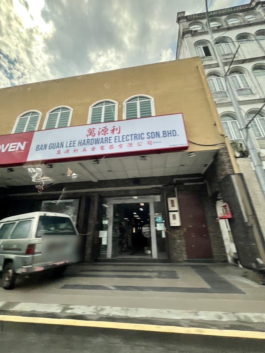 Two-storey ochre shophouse with a white signboard reading Ban Guan Lee Hardware Electric Sdn Bhd and Chinese characters, glass entrance doors under the five-foot way