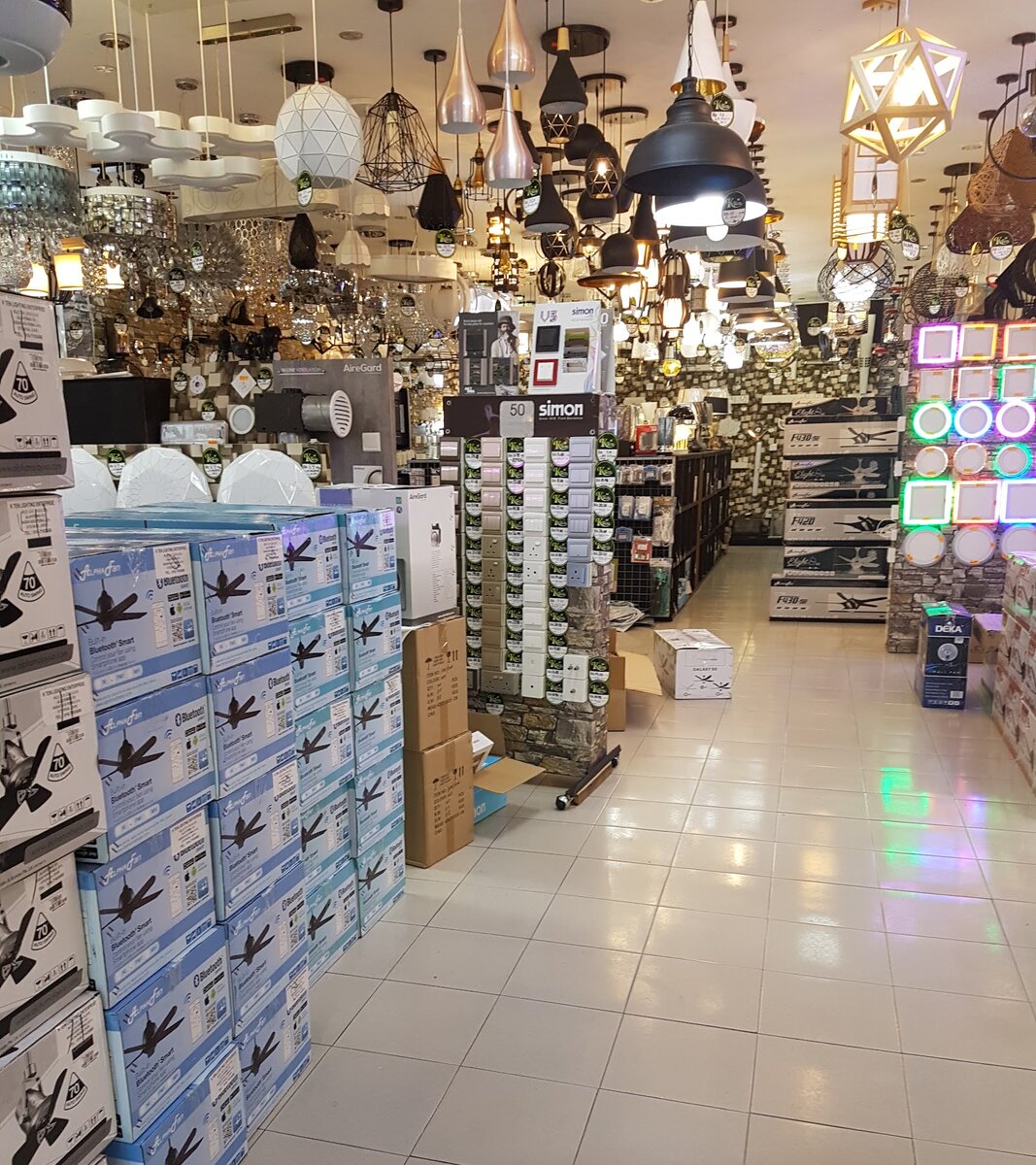 Shop aisle with pendant lights hanging from the ceiling, stacks of boxed ceiling fans and a stand of wall switches and sockets