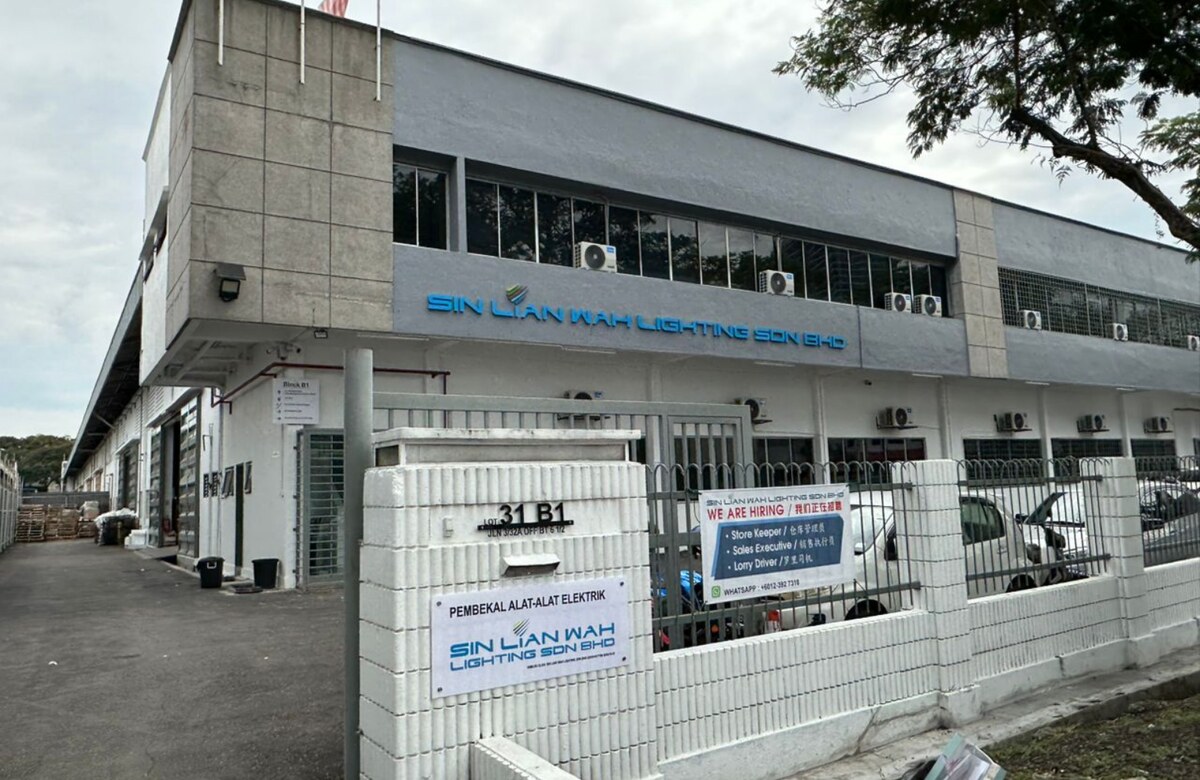 Two-storey grey and white warehouse building with Sin Lian Wah Lighting Sdn Bhd lettering, a white gate pillar marked Lot 31 B1 and a company sign on the wall