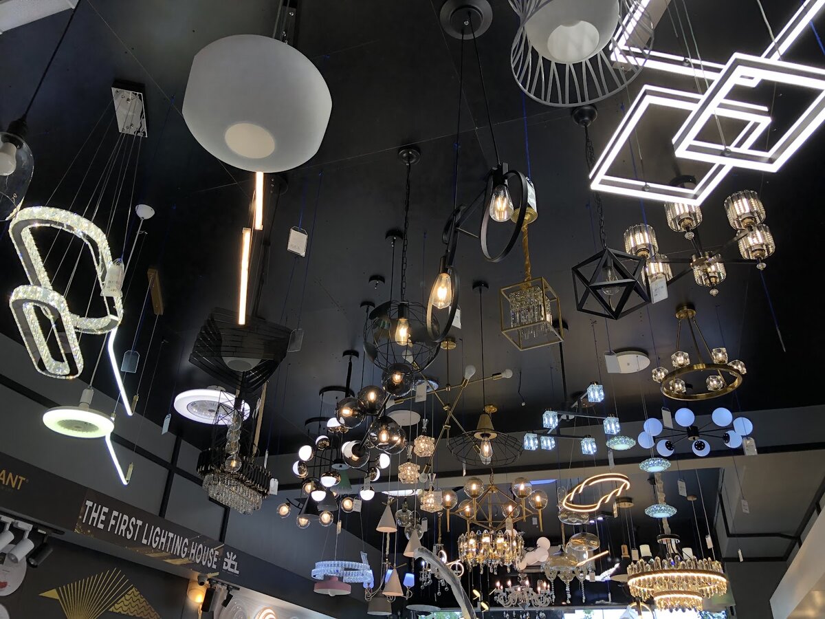 Black showroom ceiling hung with crystal chandeliers, square and ring LED pendants and glass pendant lights