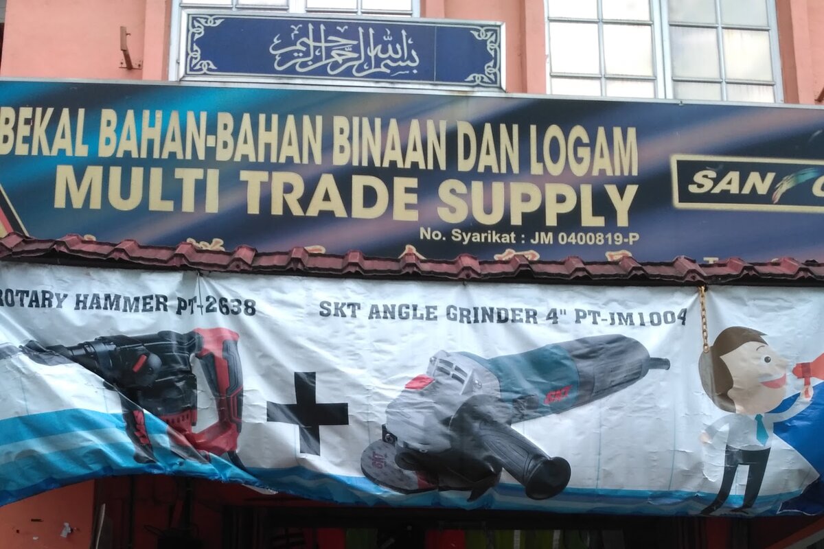 Shop signboard reading Pembekal Bahan-Bahan Binaan dan Logam Multi Trade Supply above a power-tool banner
