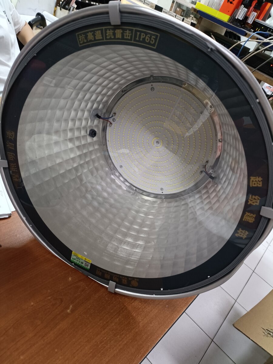 Large round LED floodlight lying on a wooden counter, its reflector facing the camera, with Chinese text and IP65 printed on the black rim