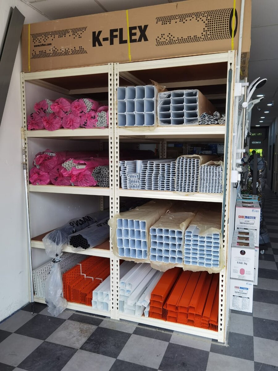 Shelving with pink-wrapped bundles of grey PVC conduit, white and orange trunking lengths, a K-Flex carton on top and Coolmaster refrigerant boxes at the side