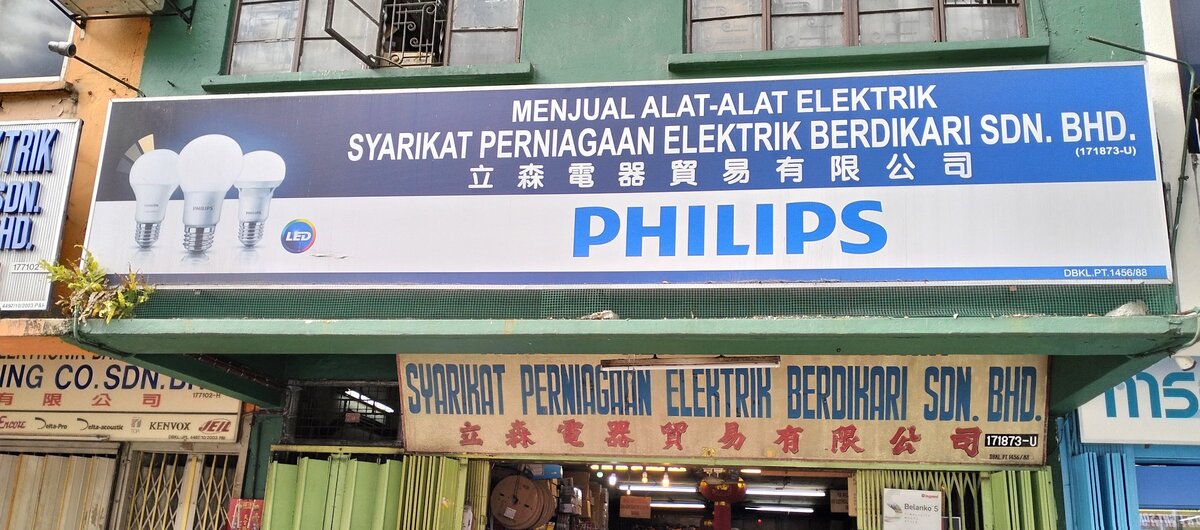 Blue and white Philips signboard reading Syarikat Perniagaan Elektrik Berdikari Sdn Bhd above an older cream signboard with blue and red lettering and an open shop doorway