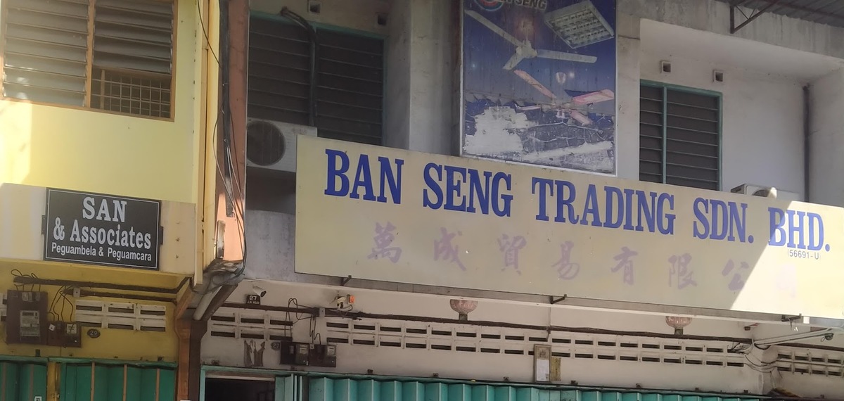 Yellow shop signboard reading Ban Seng Trading Sdn. Bhd. in blue letters with Chinese characters, below a faded poster of ceiling fans