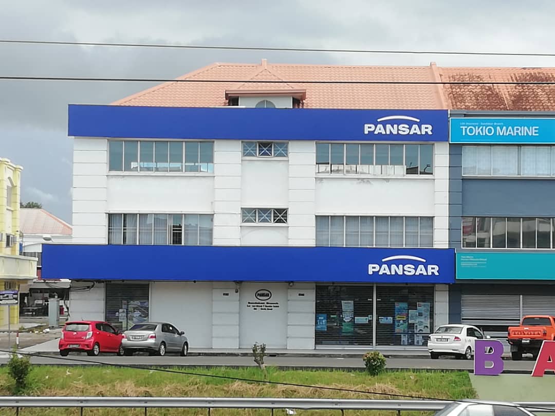 White shophouse block with two blue PANSAR fascia signs, cars parked in front