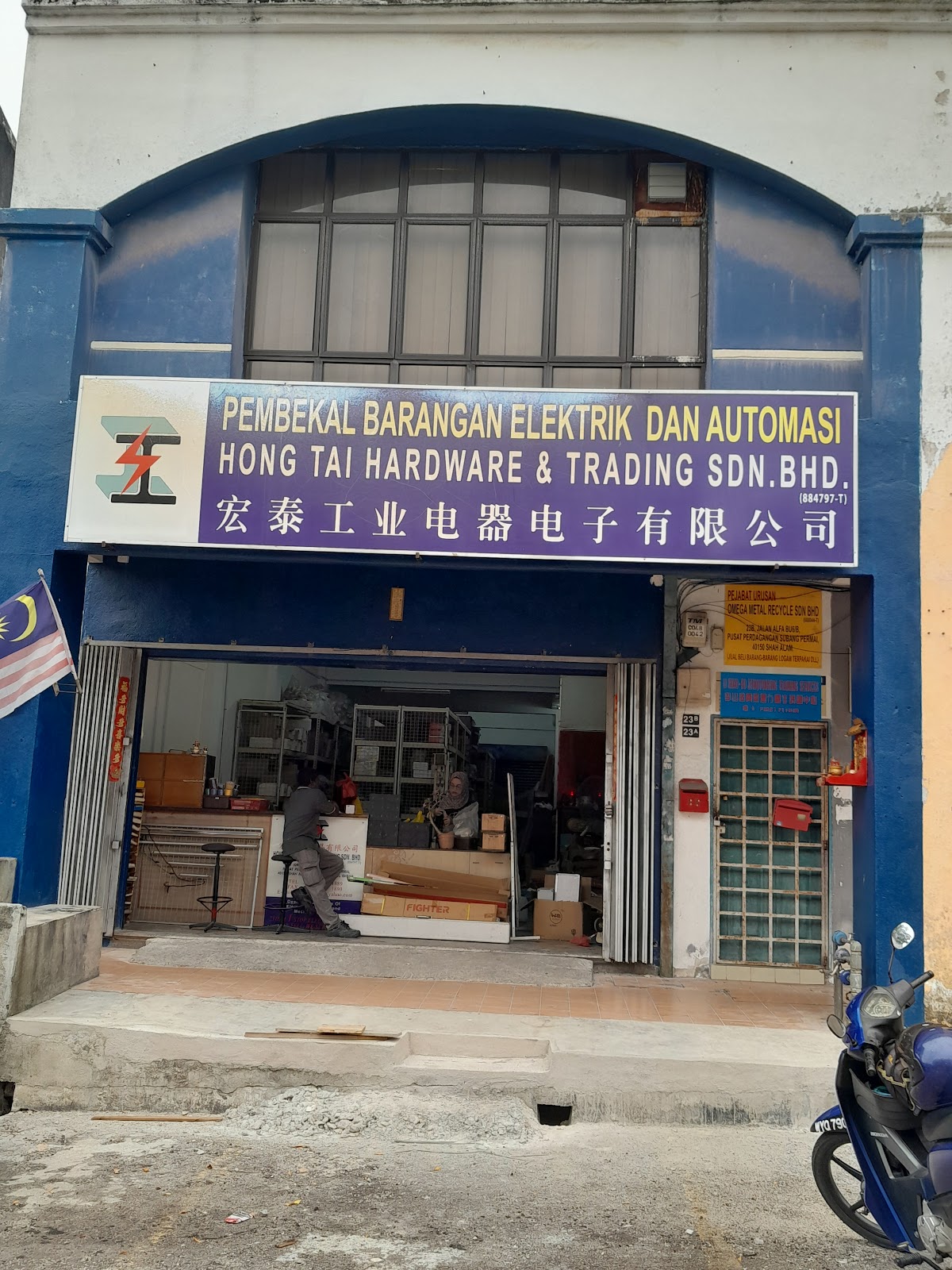 Purple signboard reading Hong Tai Hardware & Trading Sdn Bhd above an open shopfront with shelving