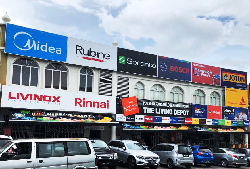 Row of shoplots with a 'Pusat Barangan Logam dan Hiasan / The Living Depot' sign and boards for Livinox, Rinnai, Nippon Paint, Jotun, Dulux and other brands