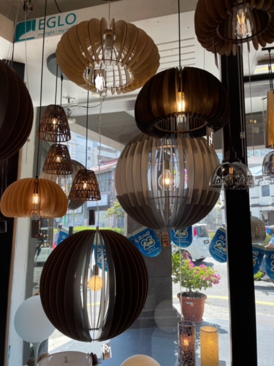 Display of hanging globe and drum pendant lamps in brown wood and smoked glass below an Eglo sign