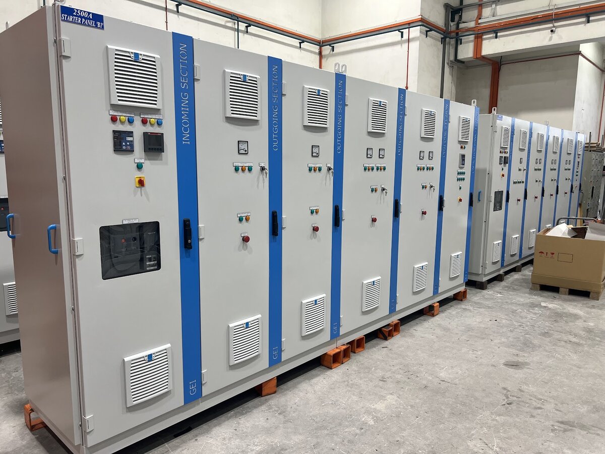 Row of grey floor-standing electrical panels with blue section doors, meters and an incoming section