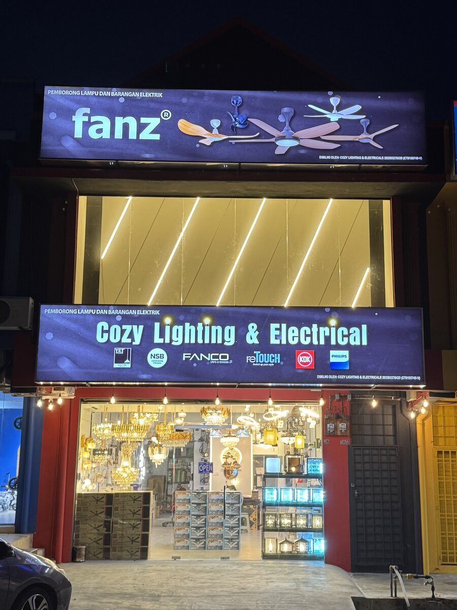 Shopfront at night with a fanz sign above a Cozy Lighting & Electrical signboard and chandeliers behind the glass