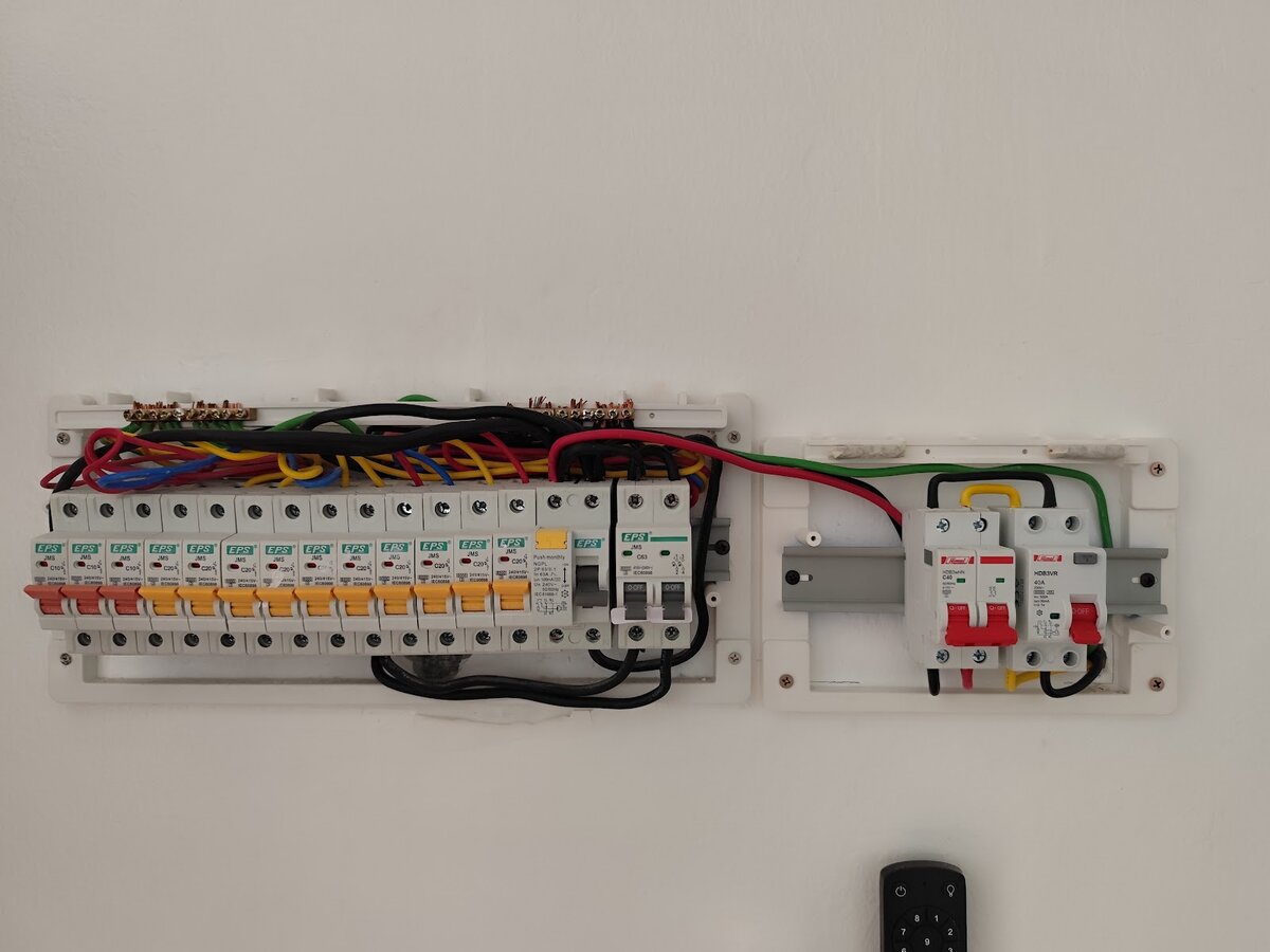Two white wall-mounted boards: on the left a row of EPS miniature circuit breakers with an RCCB and main switch, on the right a small separate board with two red-handled Himel devices, wired across with a red and black cable