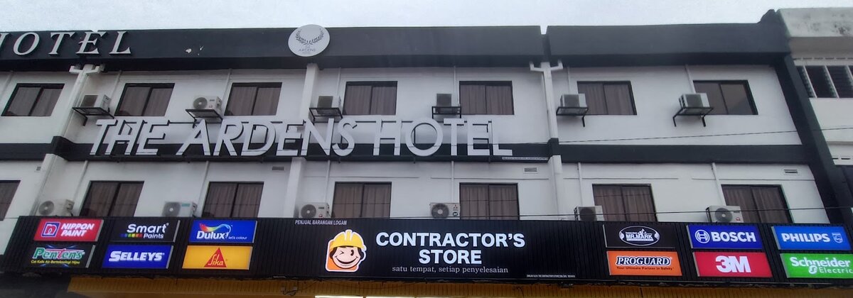 Black shop fascia reading Contractor's Store with a cartoon builder logo, flanked by Nippon Paint, Dulux, Sika, Bosch, 3M, Philips and Schneider Electric signs, below a hotel's upper floors