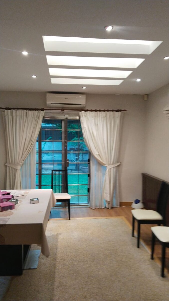 Dining room with stepped ceiling light trough panels, recessed downlights, an aircond unit above curtained glass doors, a table and chairs