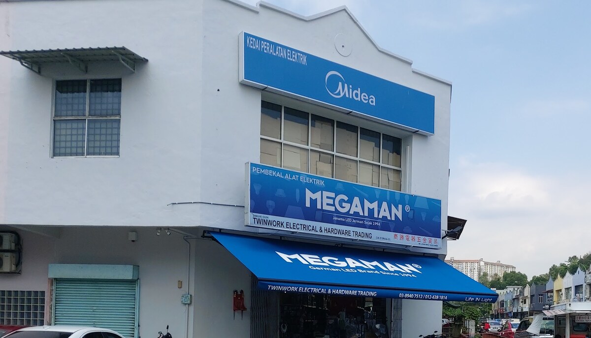 White two-storey corner shophouse with a blue Midea signboard, a blue Megaman signboard and a blue Megaman awning over an open shopfront