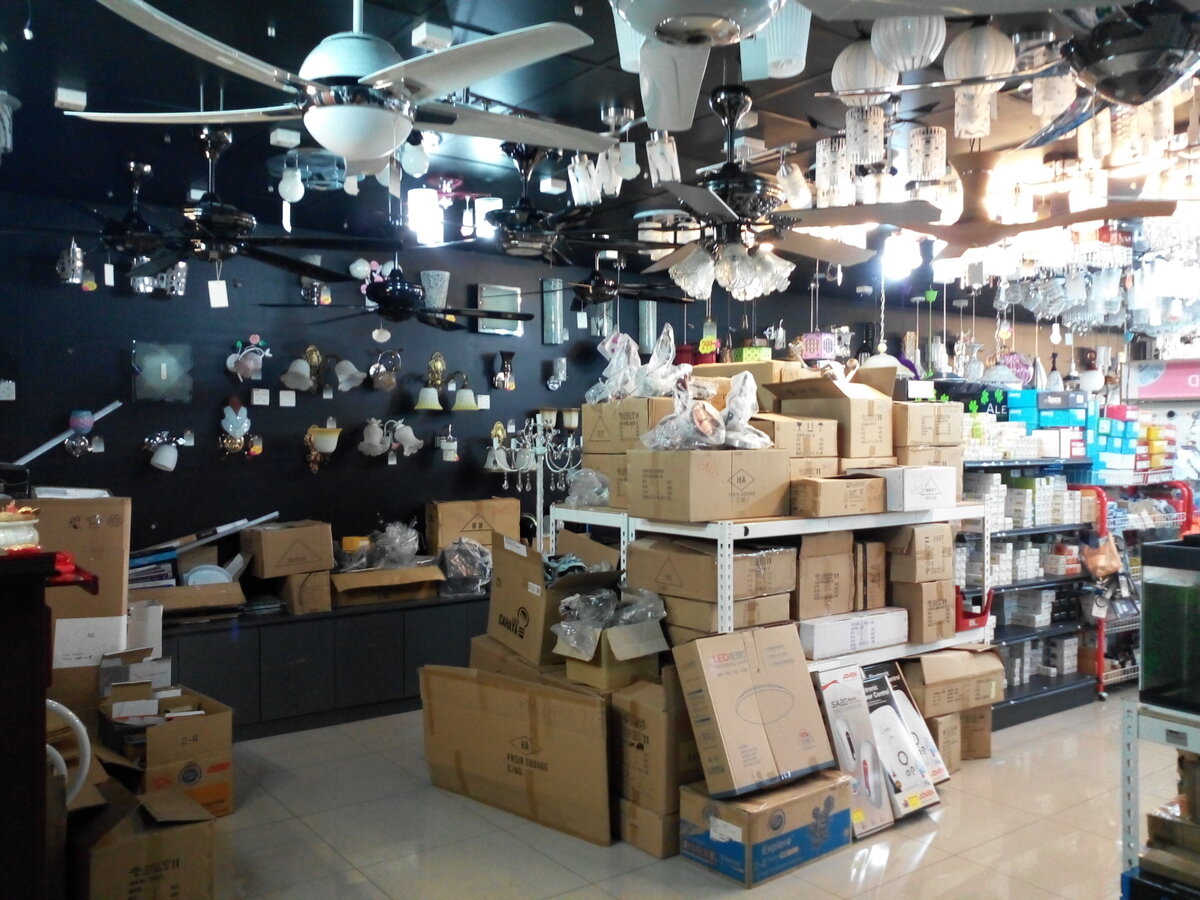 Lighting shop with ceiling fans and pendant lights overhead, wall lights on a black wall and cartons stacked on the floor
