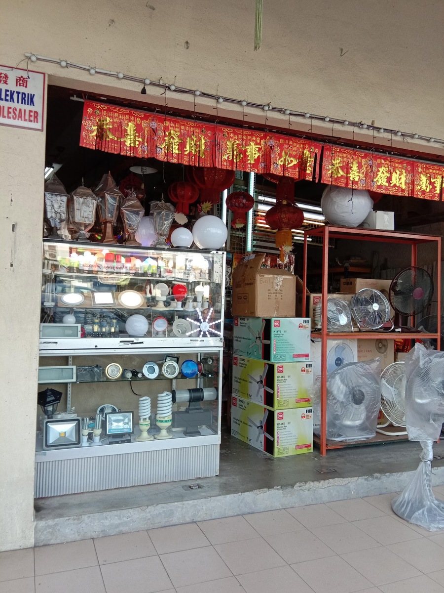 Shopfront with a glass display case of lamps and bulbs, globe lights on top, stacked KDK ceiling fan boxes and stand fans on an orange rack