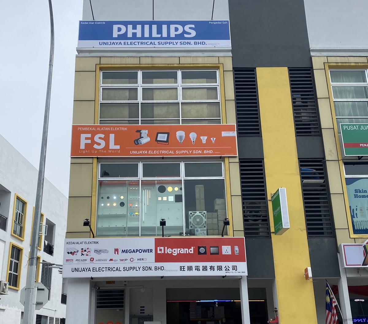 Three-storey shophouse with a blue Philips signboard at the top, an orange FSL signboard in the middle, lighting on display behind the first-floor windows and a red and white Legrand and Megapower signboard over the shop entrance