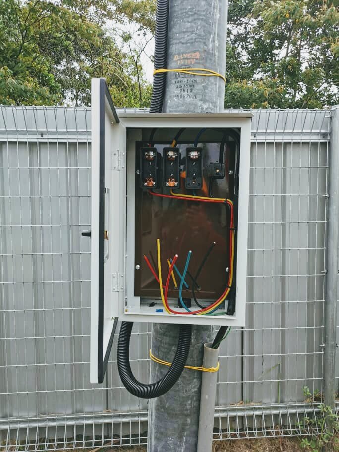 Open metal box strapped to a pole with red, yellow and blue cables entering from below
