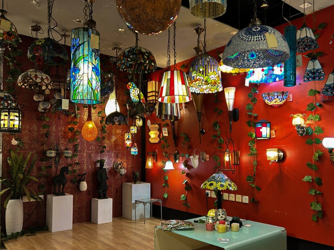 Red showroom wall hung with colourful stained-glass pendant lamps, wall lamps and a Tiffany-style table lamp