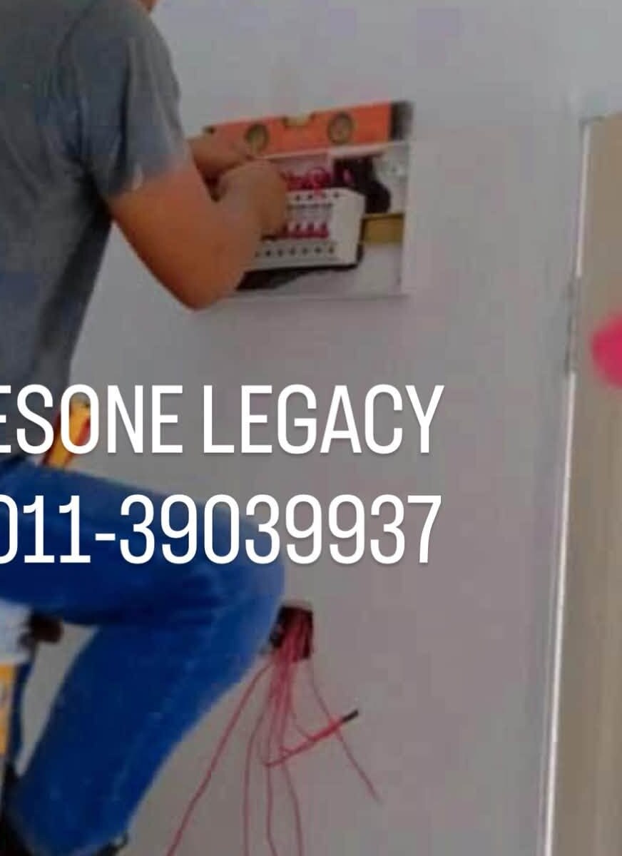 White wall with a small DB being fitted, an orange spirit level resting on it, a worker's arm and leg on the left, red cables hanging from a wall box below, and the watermark ESONE LEGACY 011-39039937