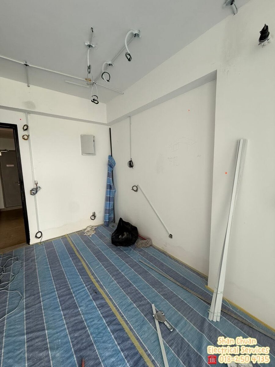 Bare apartment room with white surface conduits running across the ceiling and down the walls to cable loops, the floor covered in blue protective sheeting