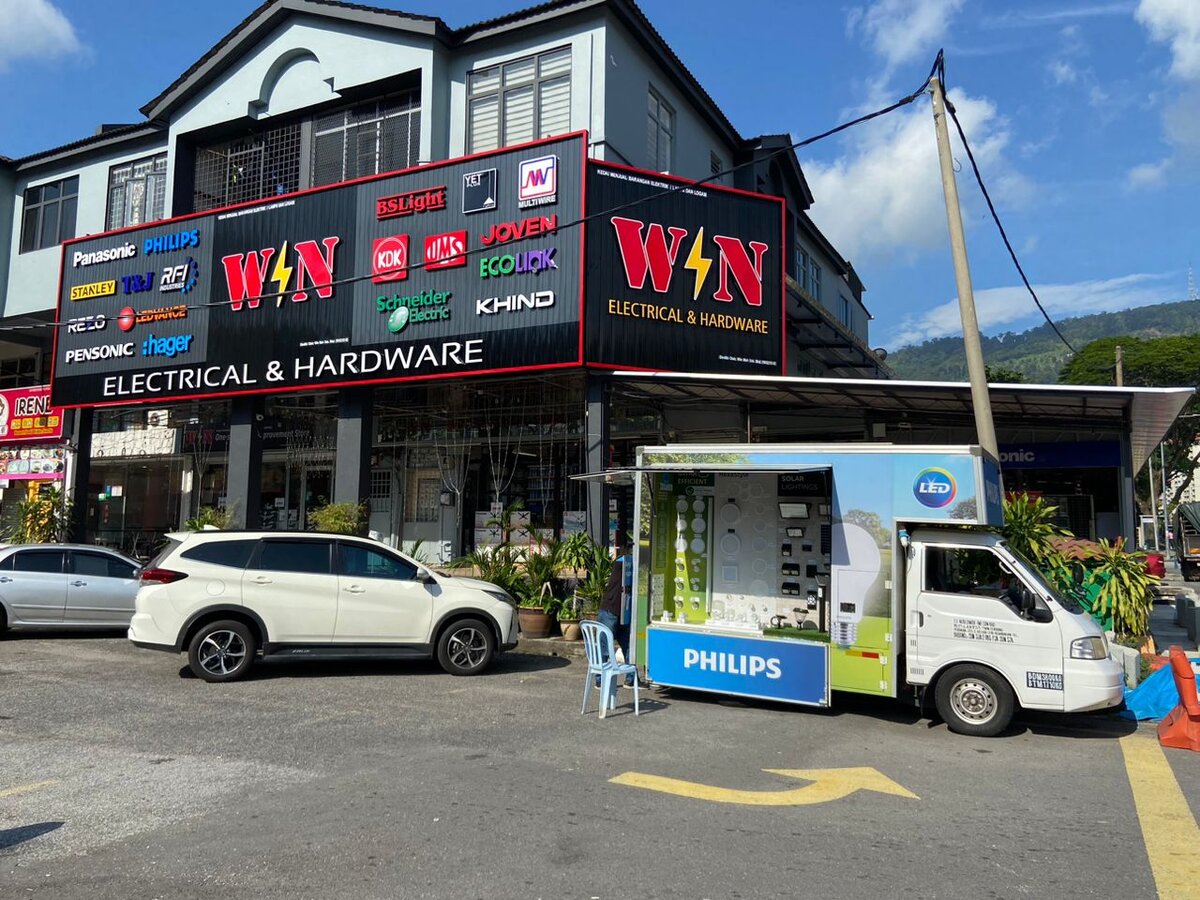 Corner shophouse with a black WIN Electrical & Hardware signboard carrying logos for Panasonic, Philips, Hager, Schneider Electric, KDK and others, a Philips-branded van parked in front