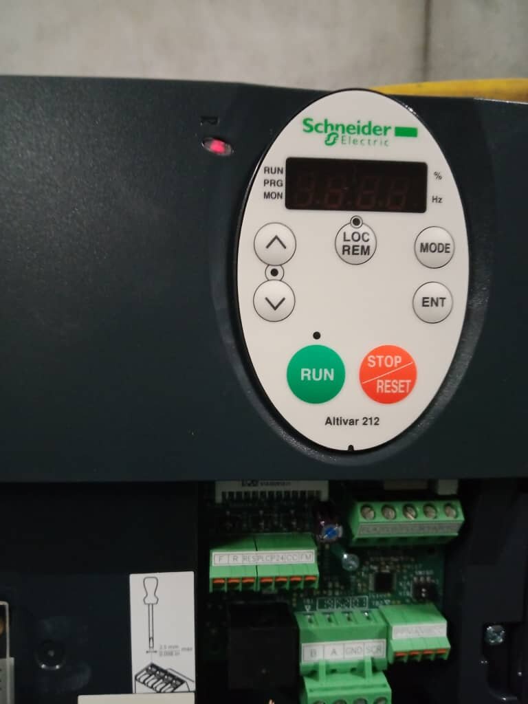 Close-up of a dark drive casing with a white Schneider Electric Altivar 212 keypad showing run and stop buttons, above green terminal blocks