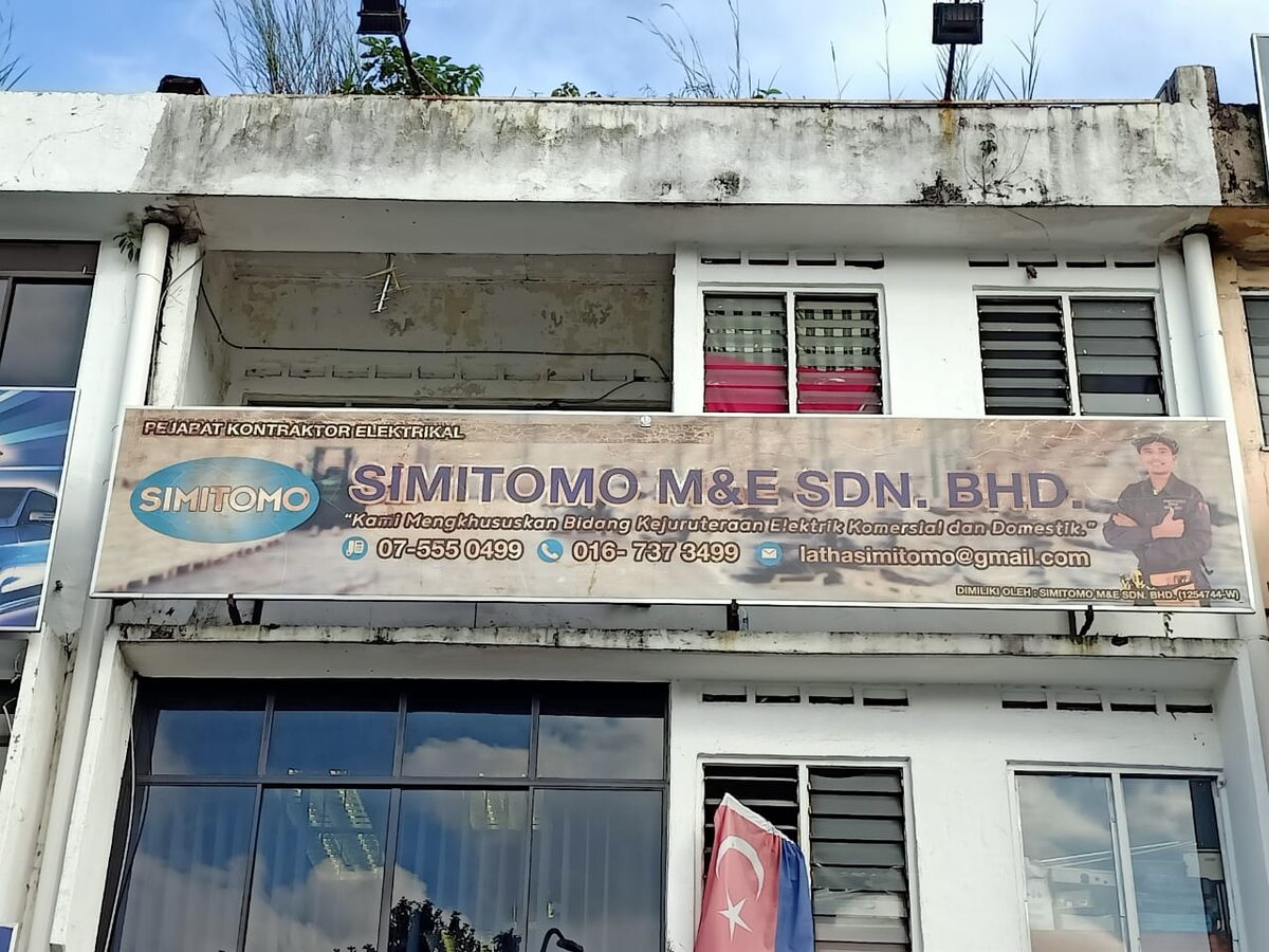 Two-storey shop lot with a long SIMITOMO M&E Sdn Bhd banner on the first floor showing phone numbers and an email address