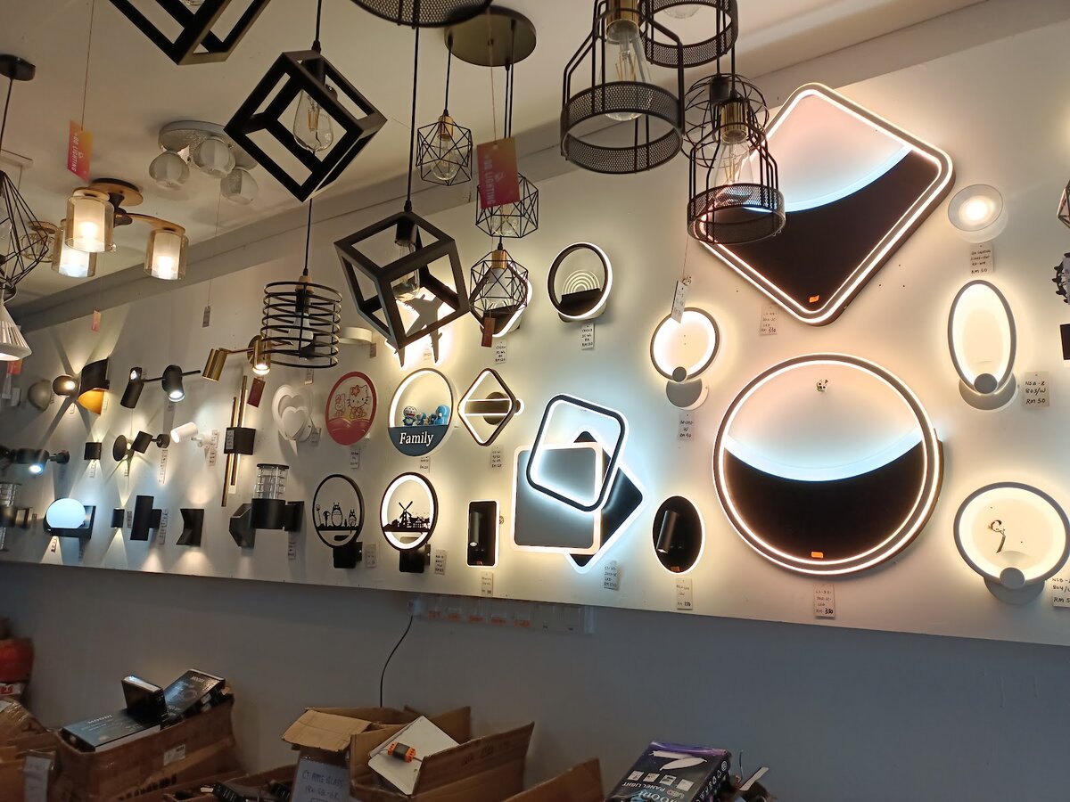 Wall of lit decorative wall lamps in rings, squares and ovals, with black cage pendants hanging above