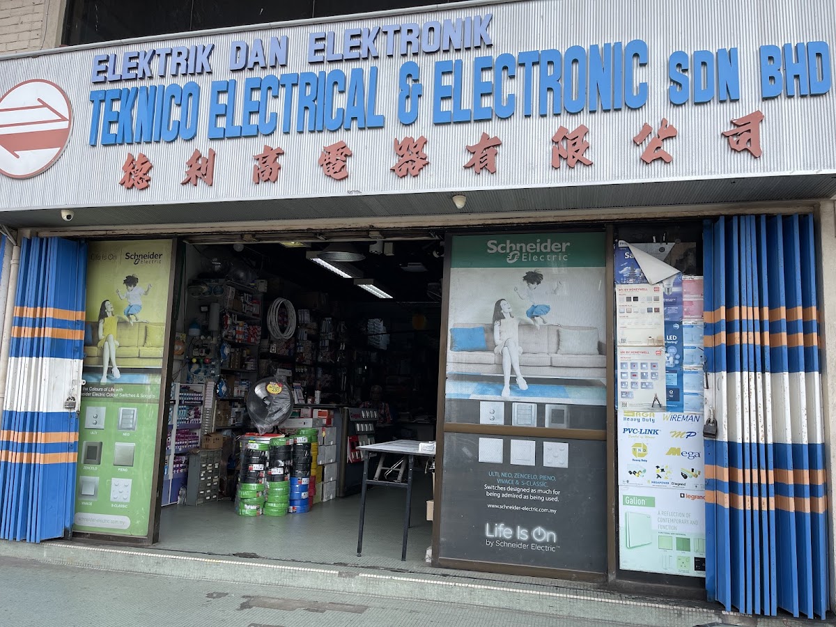 Open shopfront under a blue Teknico Electrical & Electronic signboard, with green Schneider Electric posters on both sides of the door