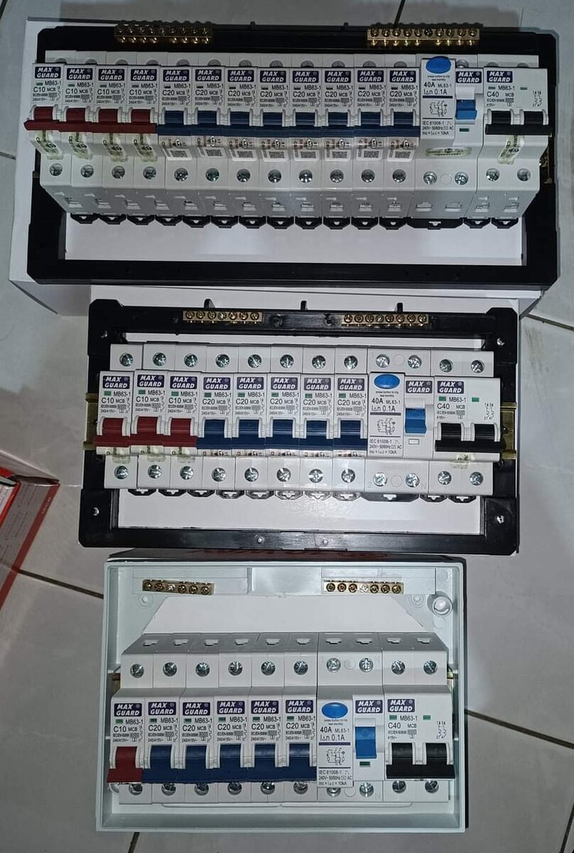Three distribution boards with rows of circuit breakers laid on a tiled floor