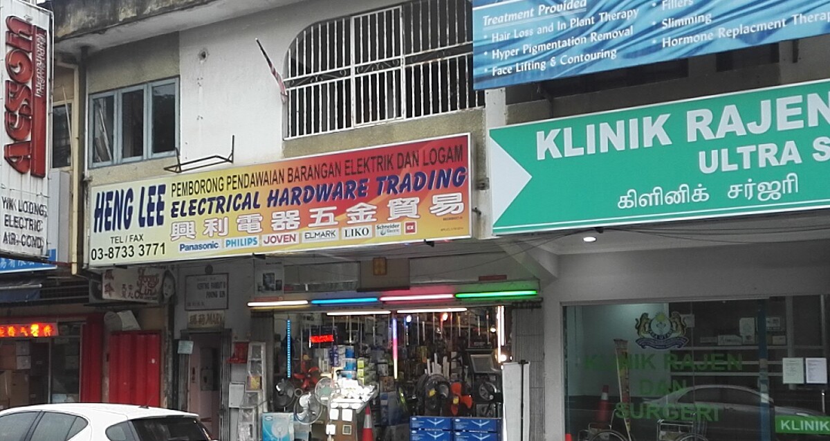 Shophouse with a yellow and orange Heng Lee Electrical Hardware Trading signboard and brand logos, fans and lamps at the open shopfront, between an aircond shop sign and a green clinic sign