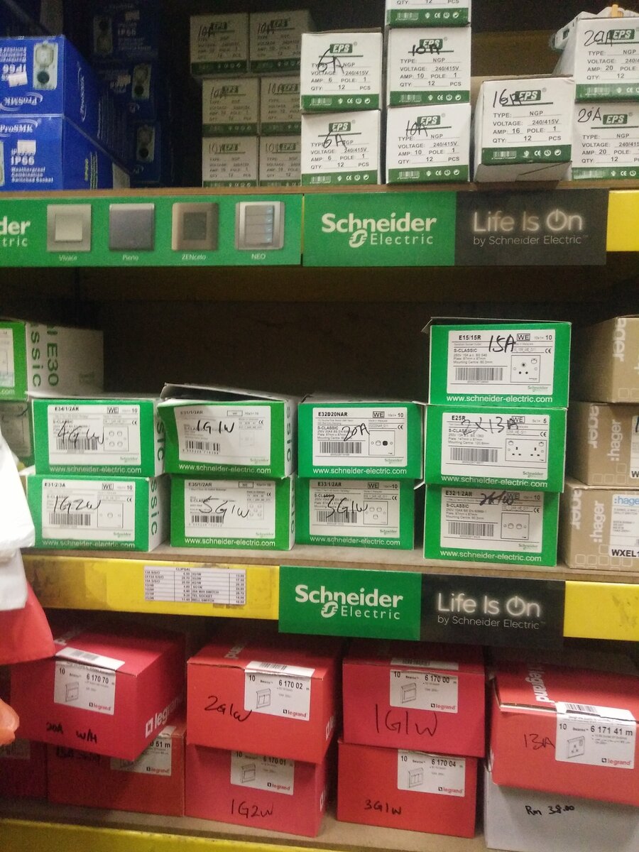 Three shelves: white EPS breaker boxes, green Schneider switch boxes under Schneider Life Is On strips, and red Legrand boxes with handwritten labels