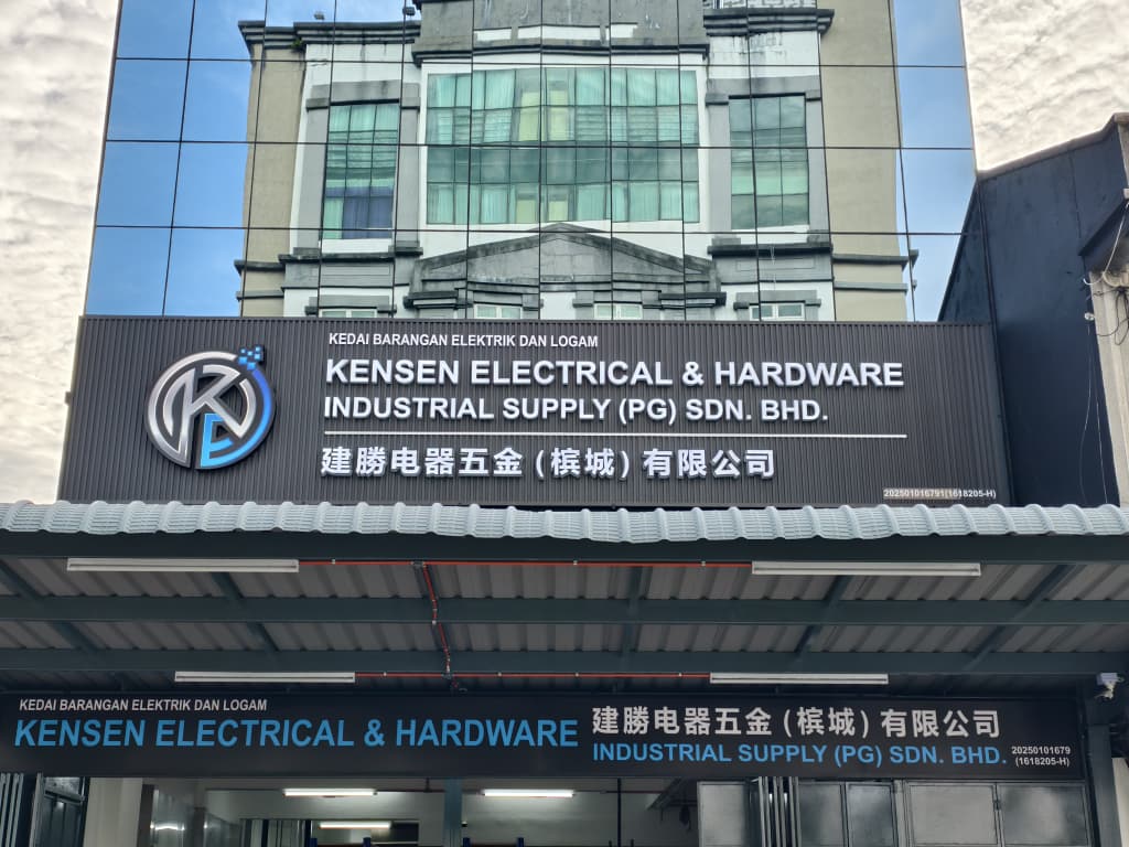 Glass-fronted building with a dark Kensen Electrical & Hardware Industrial Supply (PG) Sdn Bhd signboard, Chinese name and K logo above a covered porch with a second signboard
