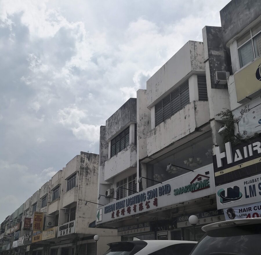 Row of weathered three-storey shophouses with a white signboard reading Khean Huat Lighting Sdn Bhd in blue and Chinese characters in red, a SmartHome logo, and pendant lights visible in a first-floor window