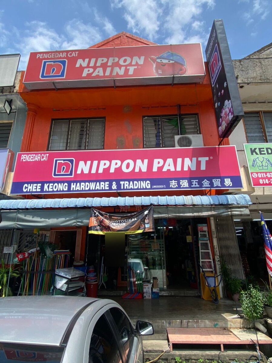 Orange shophouse with two Nippon Paint signboards, the lower one reading Chee Keong Hardware & Trading, and brooms and ladders at the entrance